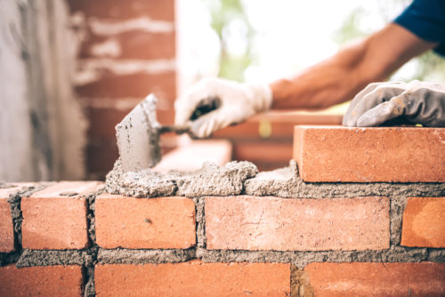 Featured image--Bricklayer worker installing brick masonry on exterior wall with trowel putty knife