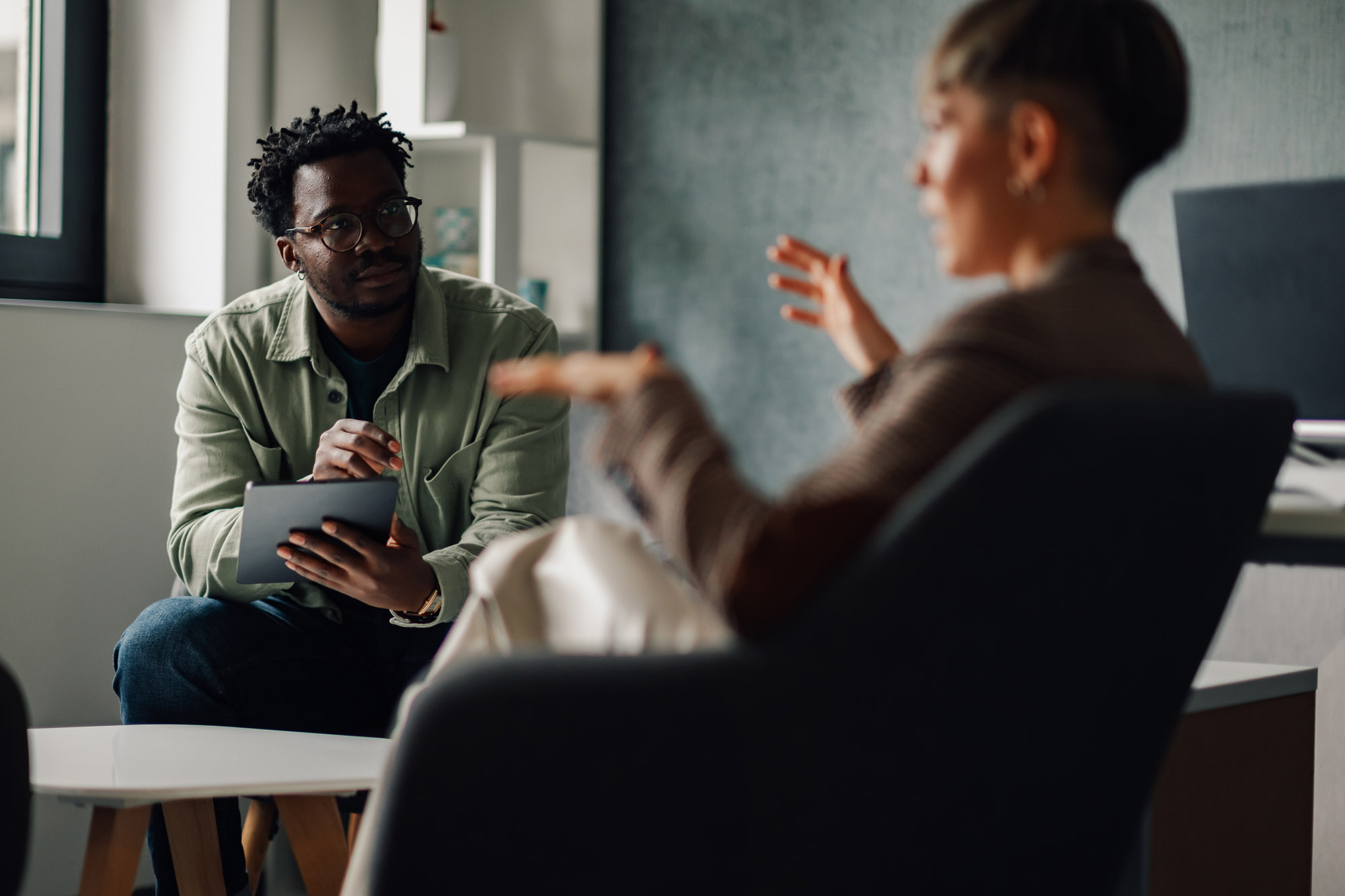 A manager talks with an employee using a tablet during a workplace discussion.